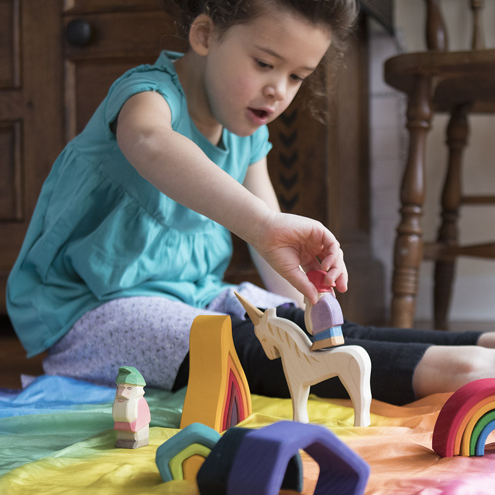 Girl playing with a wooden unicorn and a Nova Natural Rainbow Playsilk.